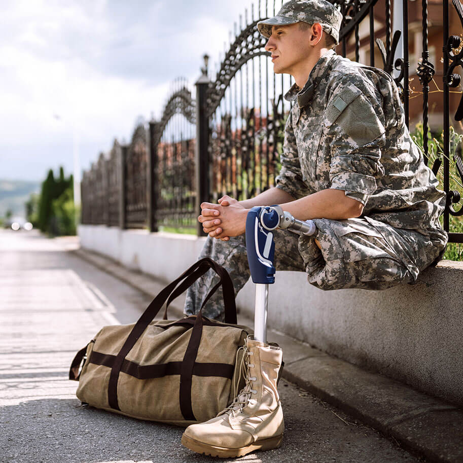 A man in military dress with a prosthetic leg waits by a road with a duffle bag. The Ohio wrongful termination military service discrimination lawyers at Horenstein, Nicholson & Blumenthal can identify when your employer broke the rules