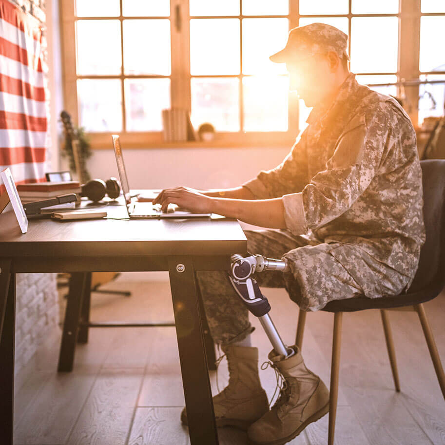 A man in military dress with prosthetic leg sits at a laptop at a table. The Ohio wrongful termination military service discrimination lawyers at Horenstein, Nicholson & Blumenthal can guide you through a legal claim.