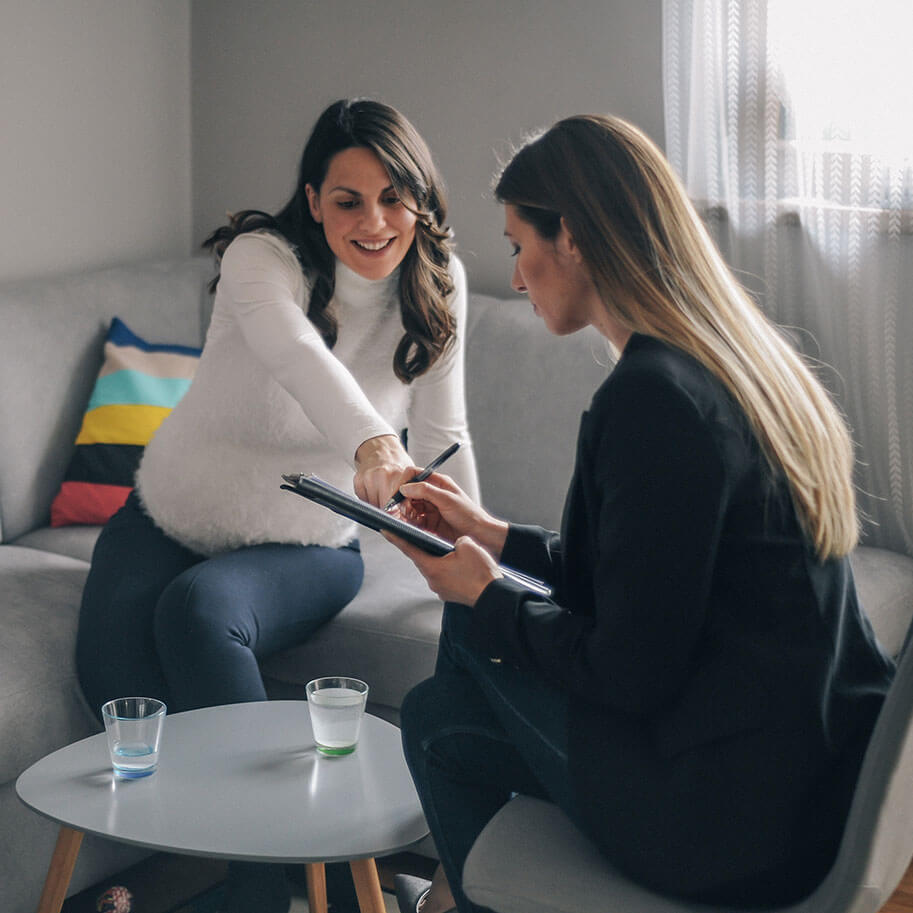 Two women talk and look at paperwork around a coffee table. The Ohio pregnancy discrimination lawyers at Horenstein, Nicholson & Blumenthal can guide you through an employment mistreatment claim.