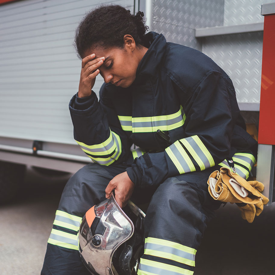 A woman in firefighting gear sits on the step of a fire truck holding her forehead in her hand. When you face risks in your government job, you can get help with workers’ compensation from Horenstein, Nicholson & Blumenthal.
