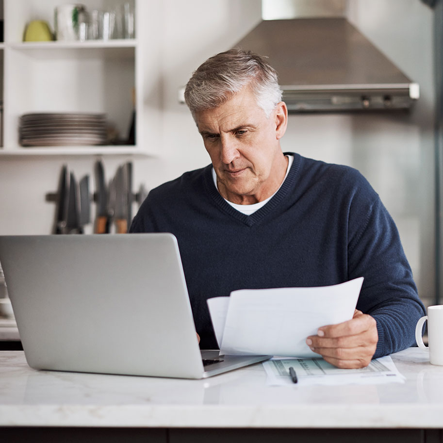 A man sits at a kitchen table looking at papers and a computer. Under aggravation of pre-existing condition law, you have to prove that your workplace injury made your health problems worse.