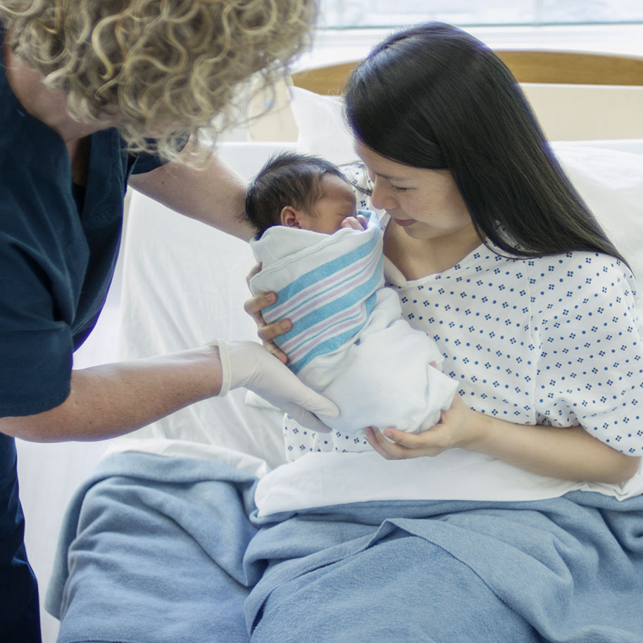 A nurse hands an infant to a woman in a hospital bed. Infant injuries can lead to lifelong, expensive care. The Ohio birth injury lawyers at HNB fight for the compensation you need.