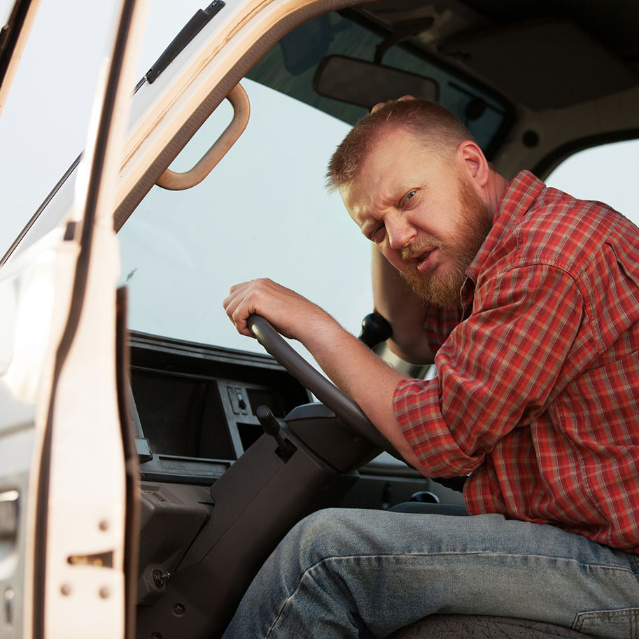 A man with a scowl on his face sits at the wheel of a semi-truck looking out an open door. Horenstein, Nicholson & Blumenthal attorneys can help you determine how much you should receive after you were injured by a big truck driver.