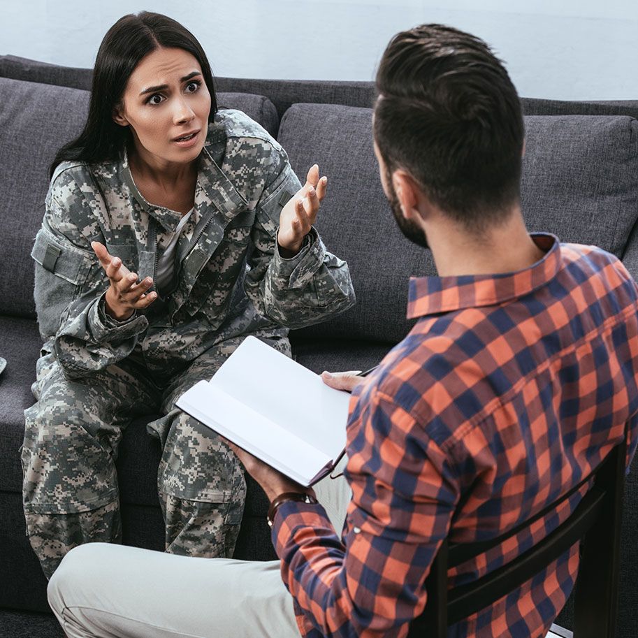 A woman in fatigues sits on a couch gesturing emphatically to a counselor. Military sexual assault attorneys from Horenstein, Nicholson & Blumenthal know how to document your MST so the VA approves financial support.