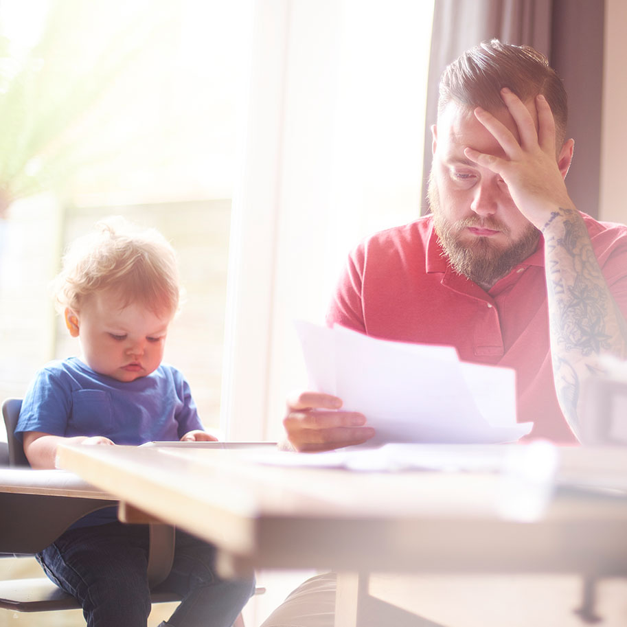A man rests his forehead in his hand while looking at papers at his dining room table next to his baby. Get a Horenstein, Nicholson & Blumenthal lawyer to be sure you’re getting maximum compensation for your truck accident injuries.