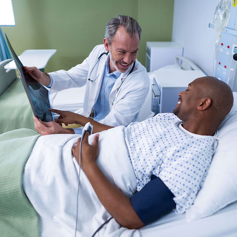 A man in a hospital bed talks to a doctor. After a work injury, a Horenstein, Nicholson & Blumenthal lawyer can make sure you receive every type of workers’ comp benefit due to you.