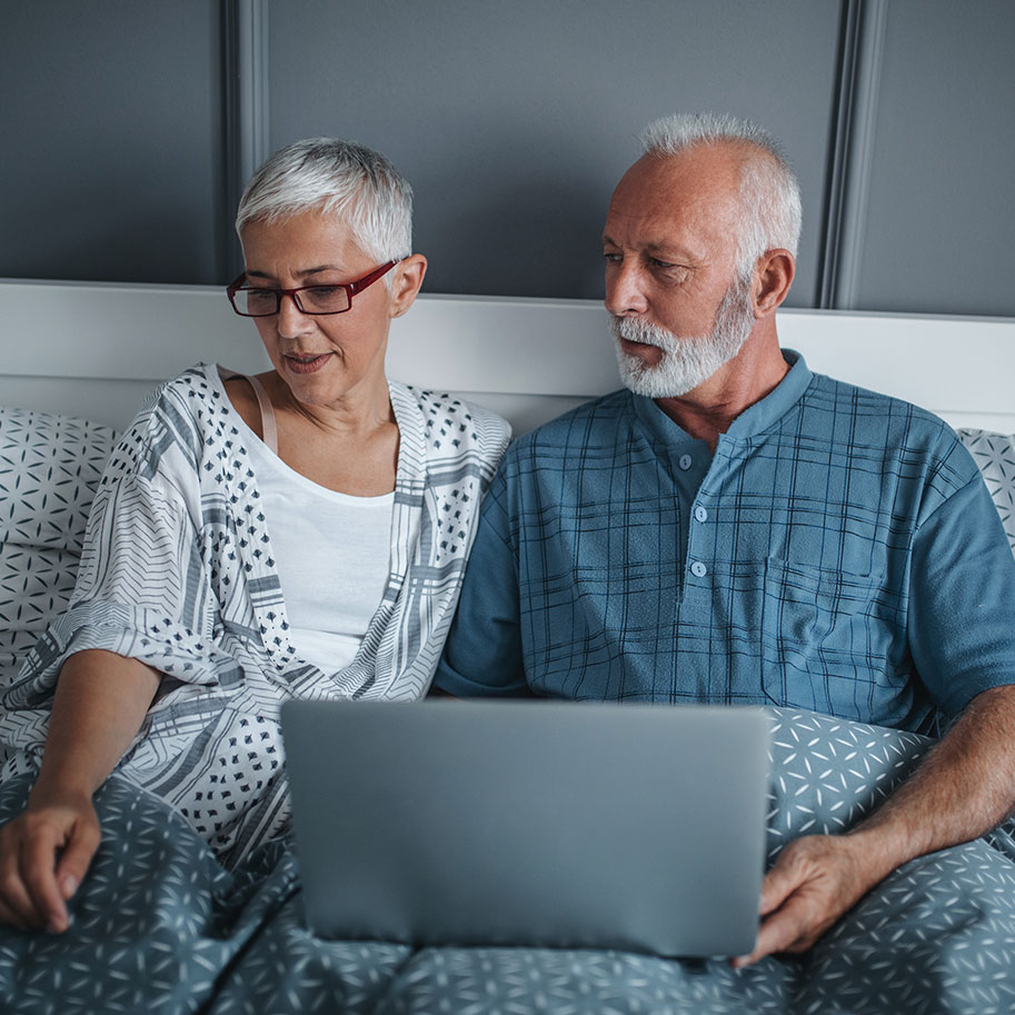 A couple sits in bed looking at a laptop computer. Getting Social Security Disability benefits for neck or back pain is complicated, but HNB knows all your options.