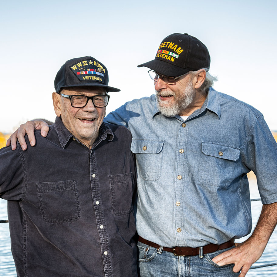 A man in a Vietnam veteran baseball cap puts his arm around another military veteran near a waterfront. Horenstein, Nicholson & Blumenthal lawyers can help you determine if your military service qualified you for Agent Orange disability payment.